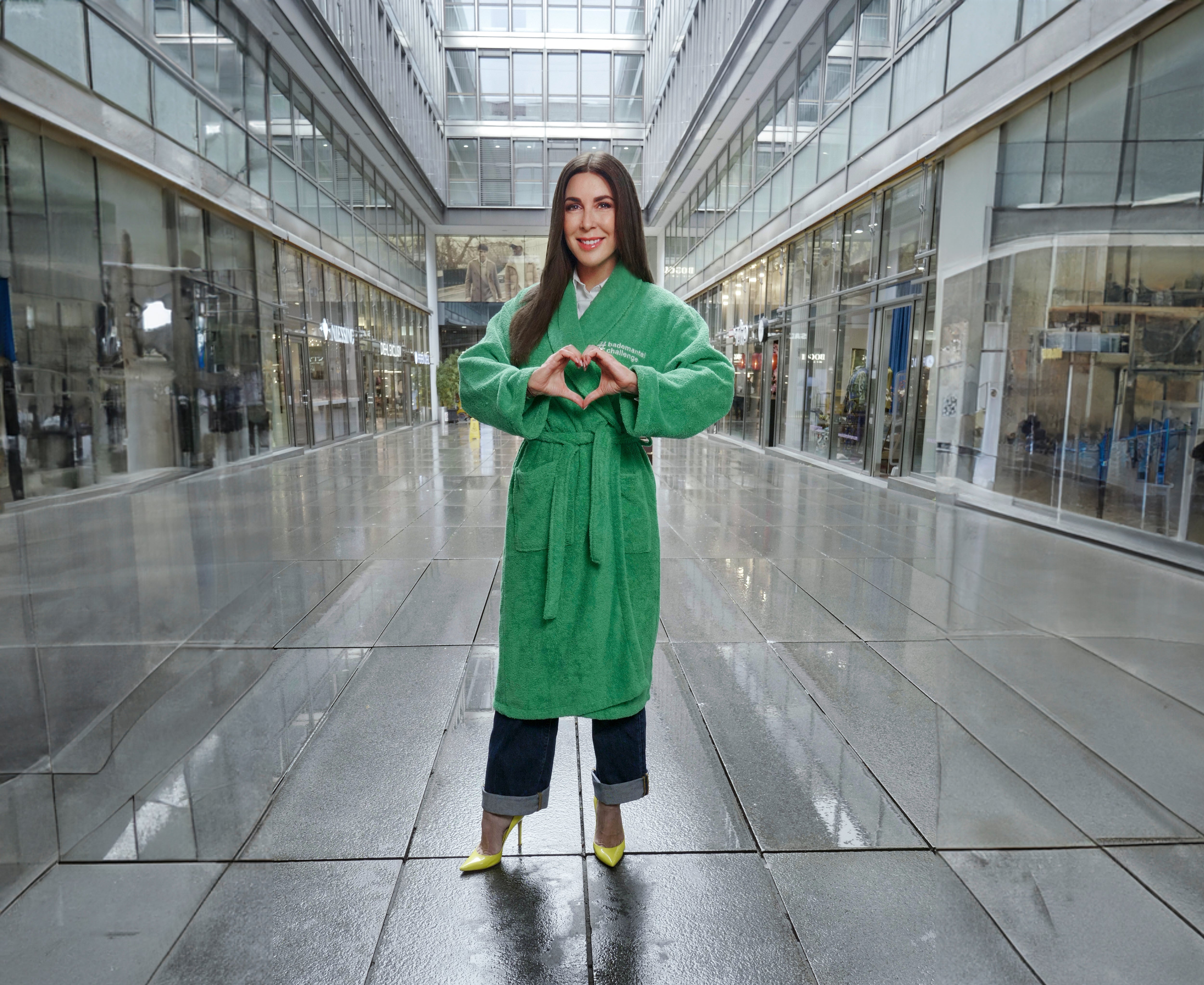 Judith Williams steht für die Kampagne der DZNE in einem grünen Bademittel mitten in einer Einkaufsstraße