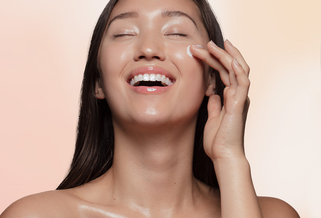 Frau, die sich lächelnd Creme auf Wange aufträgt