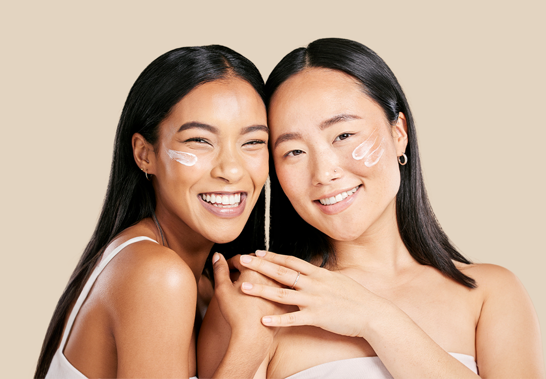 Zwei Models mit Gesichtscreme auf den Wangen, die in die Kamera lachen.